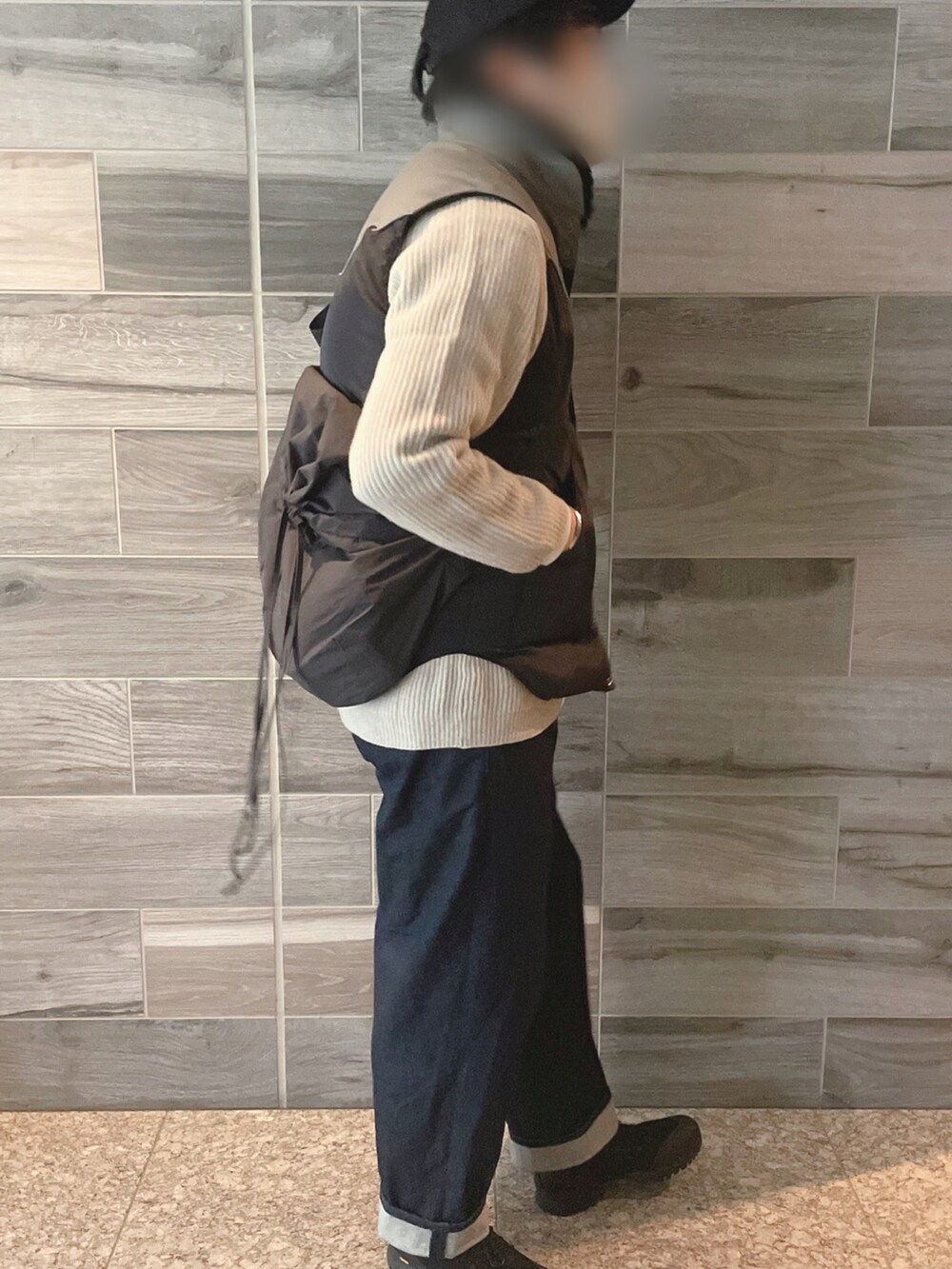 ブラウン系のダウンベスト、ホワイト系のニット/セーター、ブルー系のデニムパンツを着用したメンズの冬コーディネートの2枚目の写真