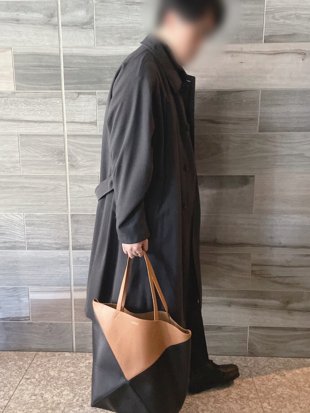 グレー系のステンカラーコート、ブラック系のニット/セーター、ブラック系のスラックスを着用したメンズの冬コーディネートの2枚目の写真