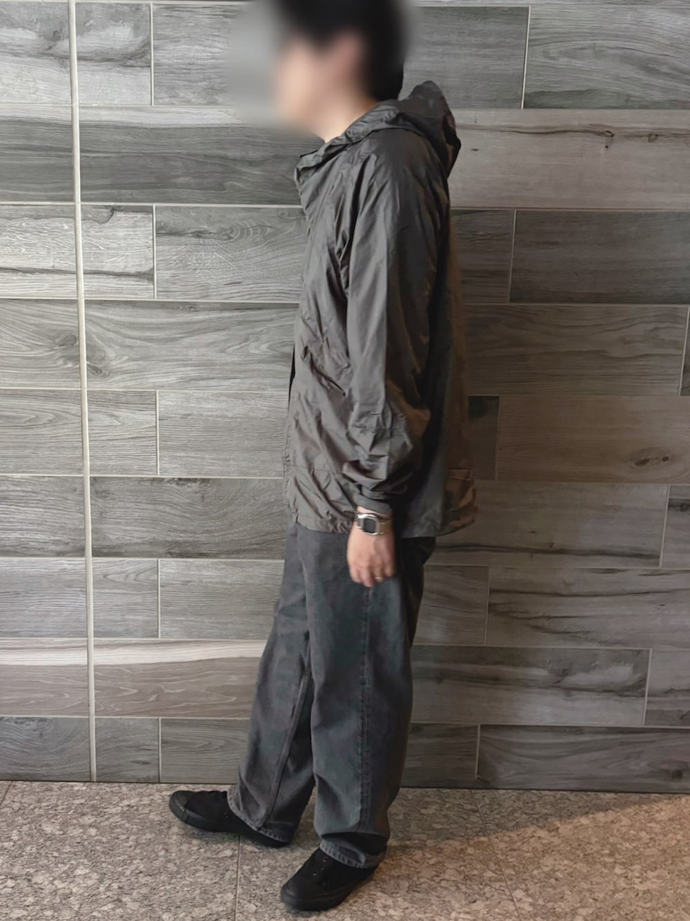 グリーン系のナイロンジャケット、グレー系のデニムパンツ、ブラック系のスニーカーを着用したメンズの秋コーディネートの2枚目の写真