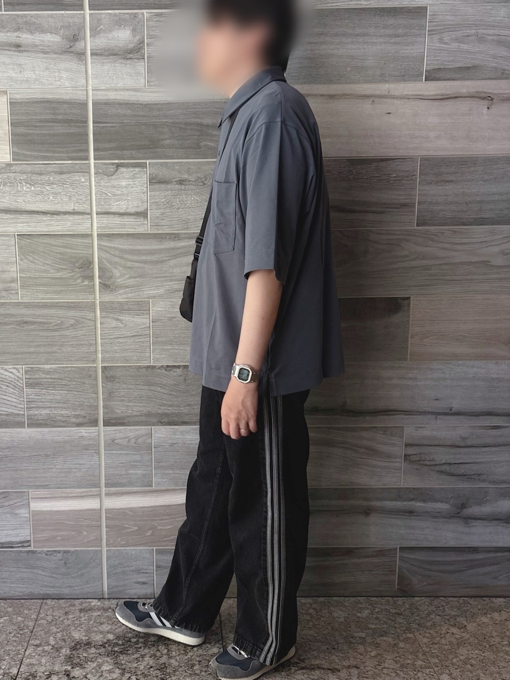 グレー系のポロシャツ、ブラック系のデニムパンツ、ブルー系のスニーカーを着用したメンズの夏コーディネートの2枚目の写真