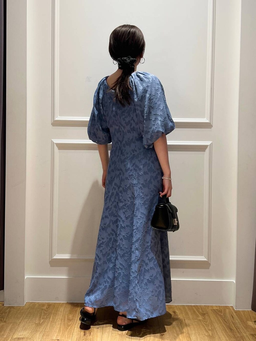 ブルー系のドレス、ブラック系のパンプス、ブラック系のショルダーバッグを着用したレディースの春コーディネートの2枚目の写真