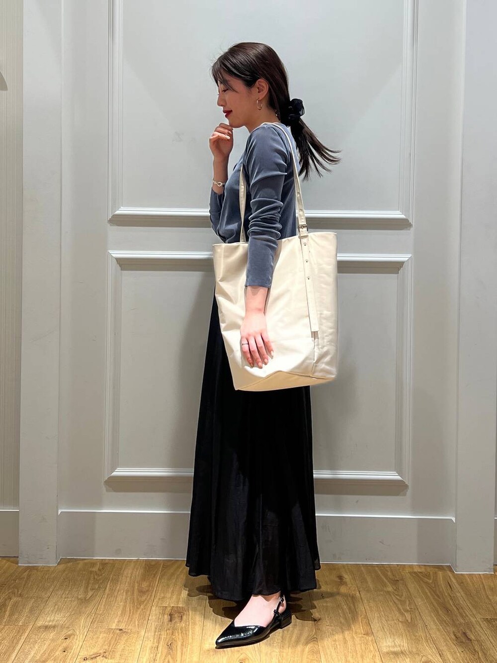 ホワイト系のトートバッグ、ブラック系のスカート、ブラック系のパンプスを着用したレディースの春コーディネートの2枚目の写真