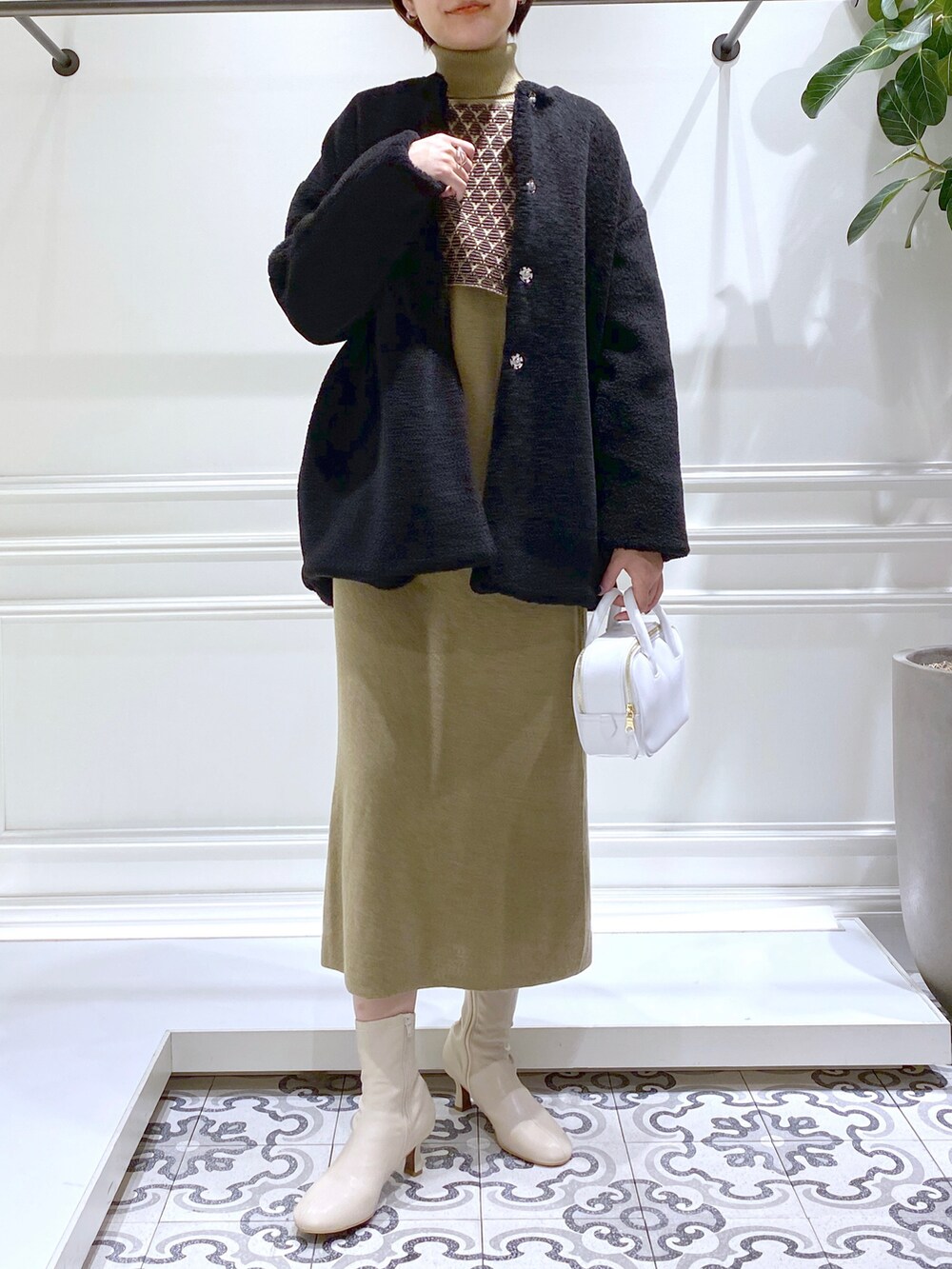 ブラック系のノーカラーコート、グリーン系のワンピース、ベージュ系のブーツを着用したレディースの秋コーディネートの2枚目の写真