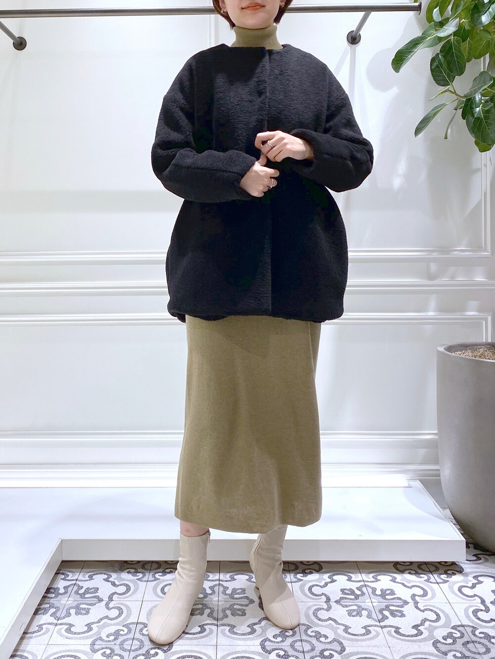 ブラック系のノーカラーコート、グリーン系のワンピース、ベージュ系のブーツを着用したレディースの秋コーディネートの5枚目の写真