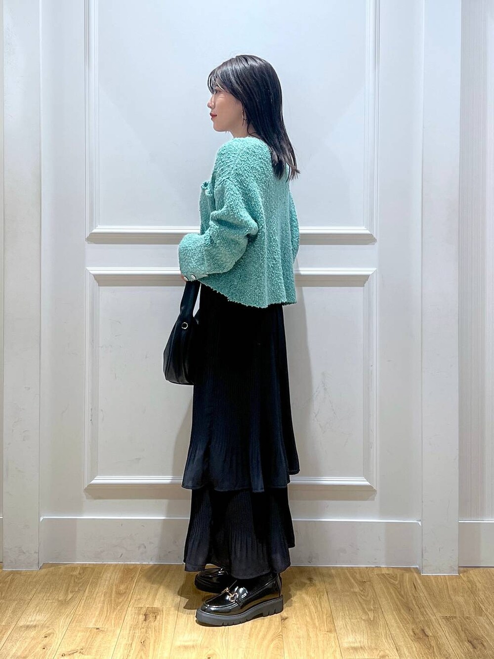 グリーン系のカーディガン/ボレロ、ブラック系のスカート、ブラック系のハンドバッグを着用したレディースの秋コーディネートの2枚目の写真