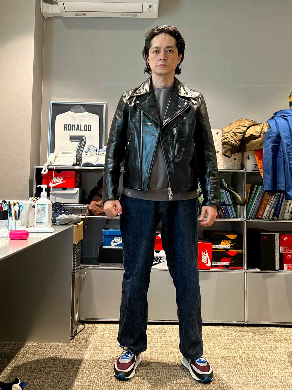 ブラック系のライダースジャケット、ブルー系のデニムパンツ、その他のスニーカーを着用したメンズの春コーディネートの2枚目の写真