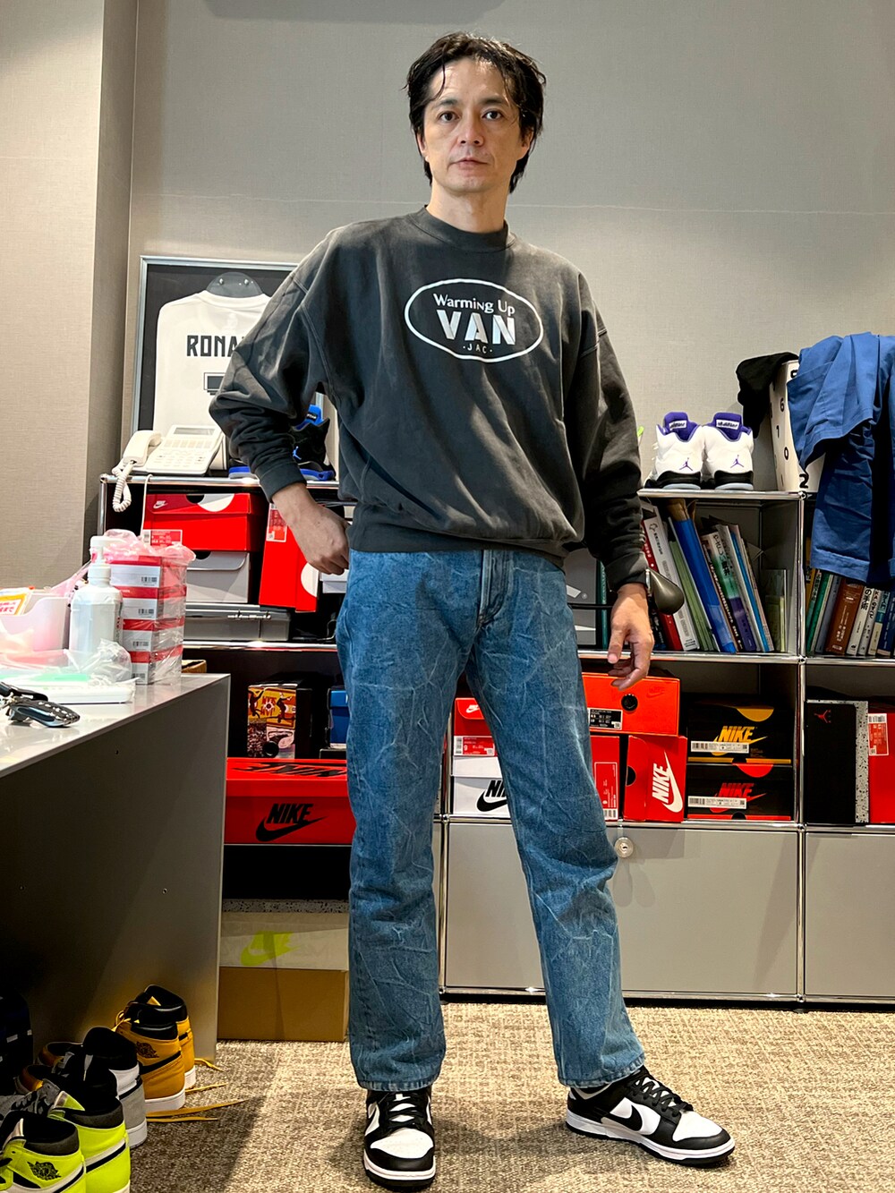 グレー系のスウェット、ブルー系のデニムパンツ、ブラック系のスニーカーを着用したメンズの秋コーディネートの4枚目の写真