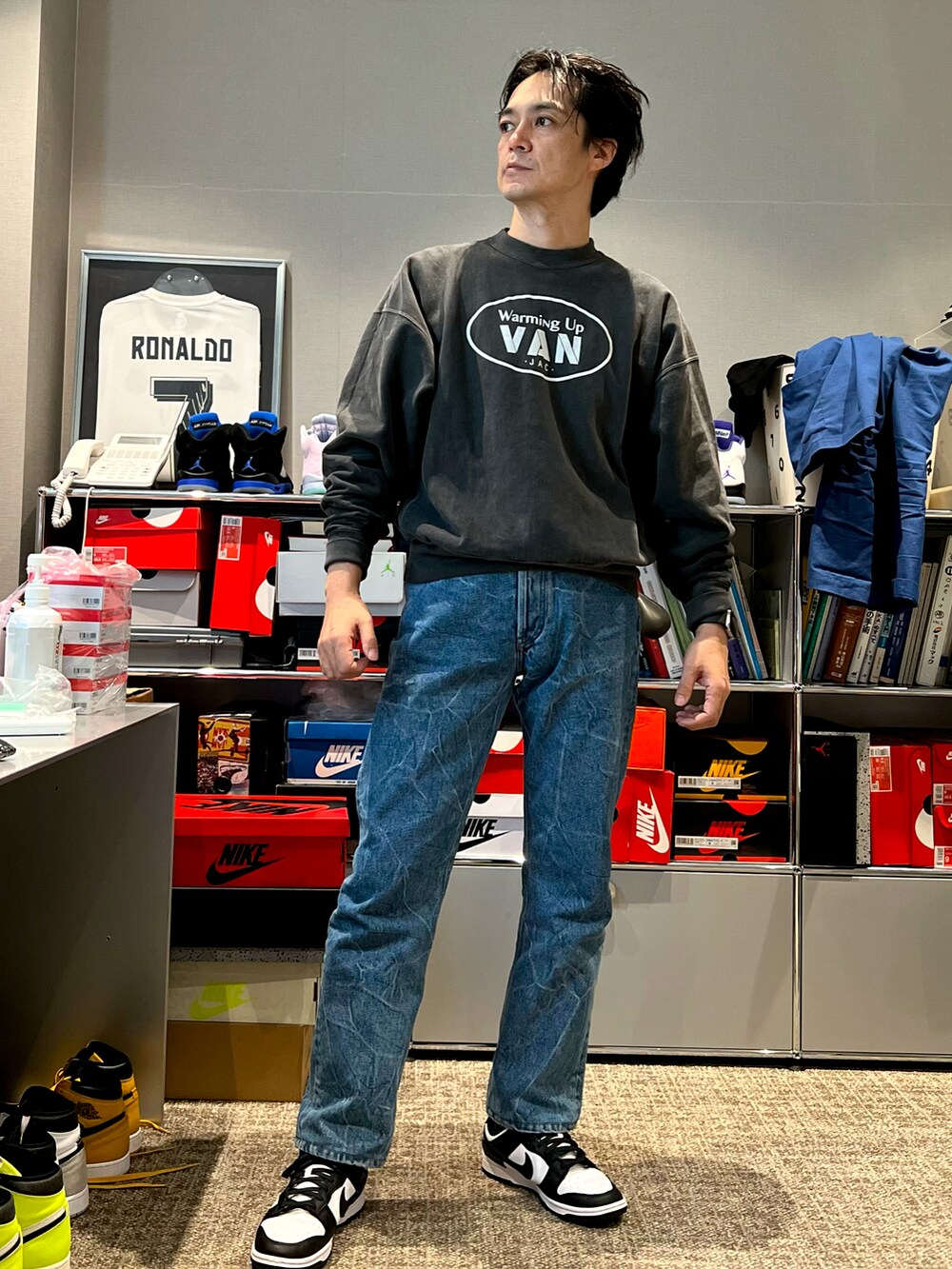 グレー系のスウェット、ブルー系のデニムパンツ、ブラック系のスニーカーを着用したメンズの秋コーディネートの2枚目の写真