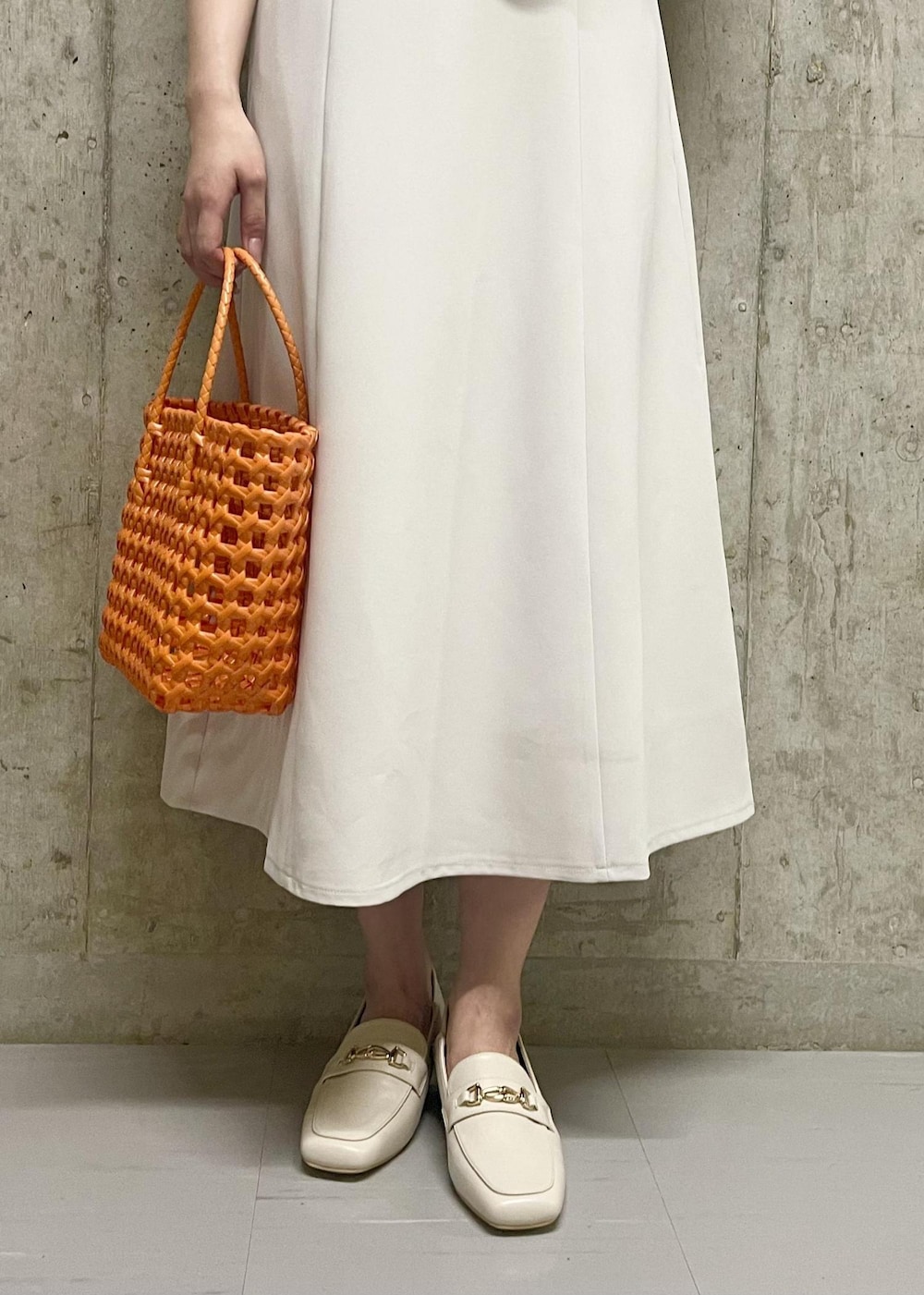 オレンジ系のトートバッグ、ホワイト系のローファー、ホワイト系のニット/セーターを着用したレディースの夏コーディネートの5枚目の写真