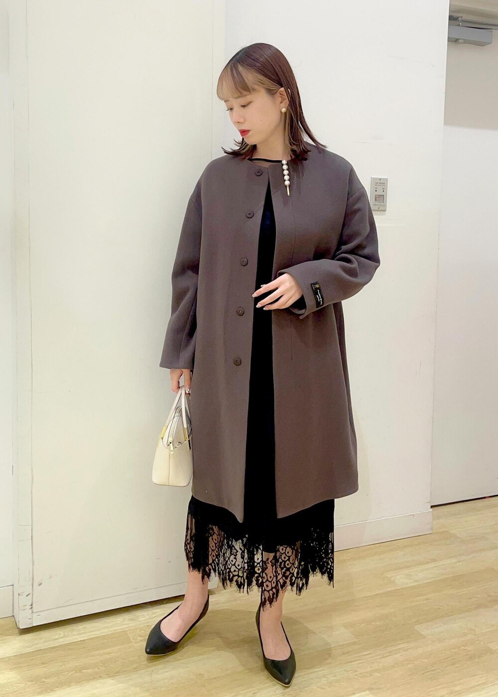 ブラック系のドレス、ブラック系のパンプス、ホワイト系のショルダーバッグを着用したレディースの冬コーディネートの2枚目の写真