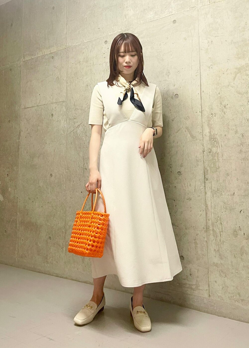 オレンジ系のトートバッグ、ホワイト系のローファー、ホワイト系のニット/セーターを着用したレディースの夏コーディネートの2枚目の写真