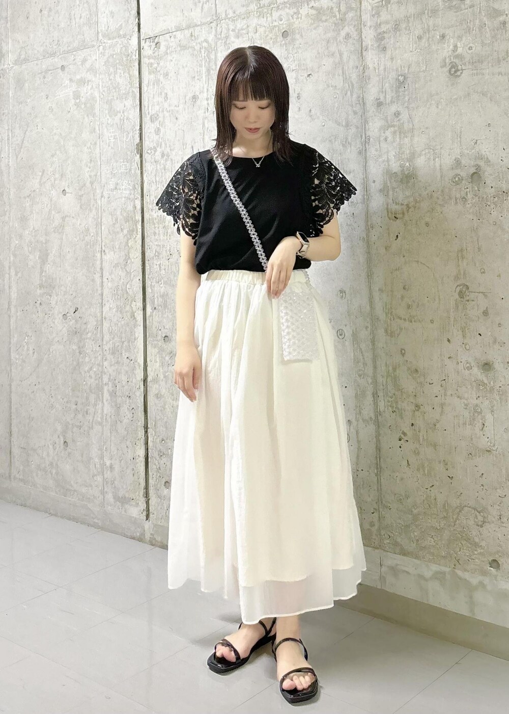 ホワイト系のスカート、ブラック系のTシャツ/カットソー、ブラック系のサンダルを着用したレディースの夏コーディネートの2枚目の写真