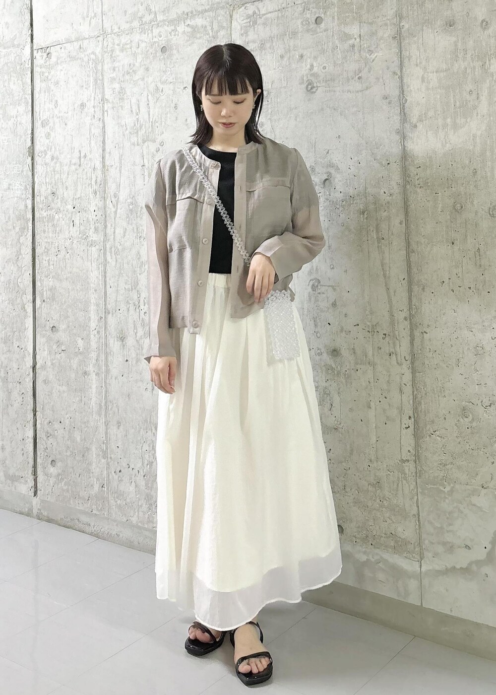 ホワイト系のスカート、ベージュ系のカーディガン/ボレロ、ブラック系のTシャツ/カットソーを着用したレディースの夏コーディネートの2枚目の写真