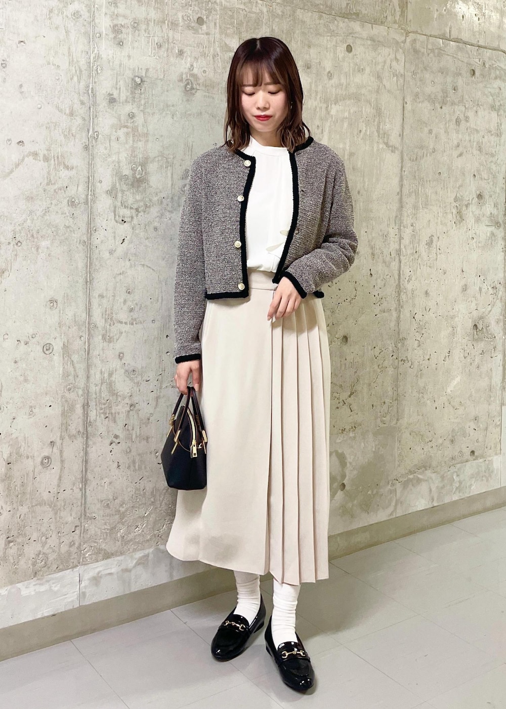 ブラック系のローファー、ブラック系のショルダーバッグ、ベージュ系のスカートを着用したレディースの春コーディネートの2枚目の写真