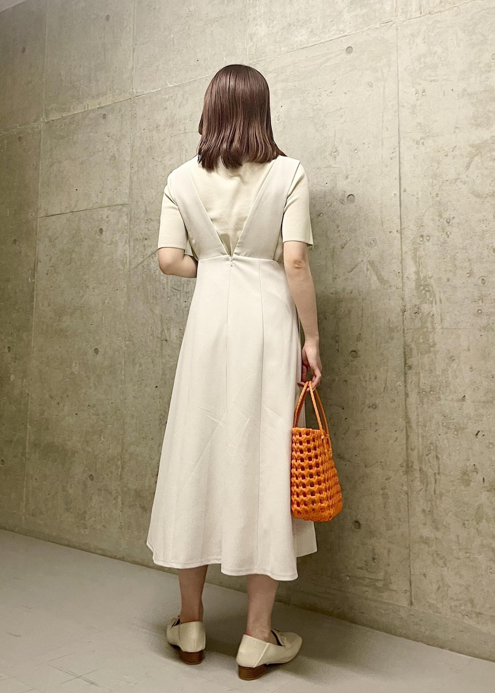 オレンジ系のトートバッグ、ホワイト系のローファー、ホワイト系のニット/セーターを着用したレディースの夏コーディネートの3枚目の写真