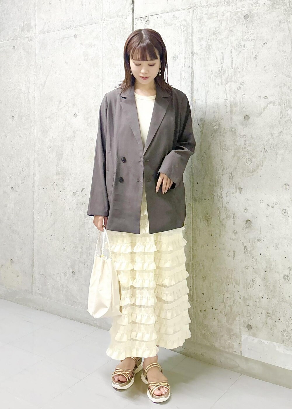 ホワイト系のワンピース、ゴールド系のサンダル、ブラウン系のテーラードジャケットを着用したレディースの夏コーディネートの3枚目の写真