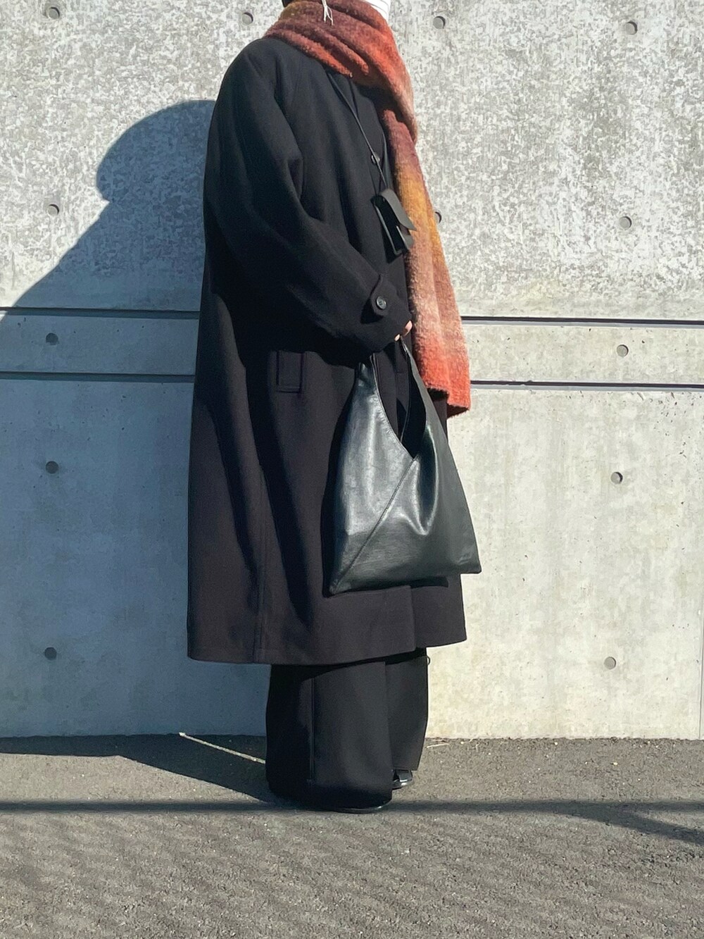 ブラック系のステンカラーコート、ブラック系のトートバッグ、ブラック系のスラックスを着用したメンズの冬コーディネートの2枚目の写真