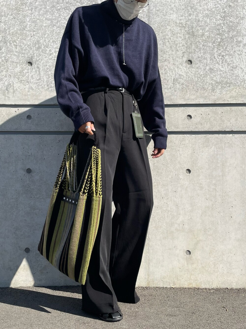 グリーン系のトートバッグ、ブルー系のニット/セーター、ブラック系のスラックスを着用したメンズの秋コーディネートの3枚目の写真