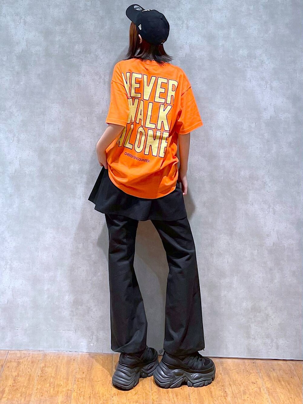 ブラック系のスニーカー、オレンジ系のTシャツ/カットソー、ブラック系のチノパンツを着用したレディースの夏コーディネートの2枚目の写真