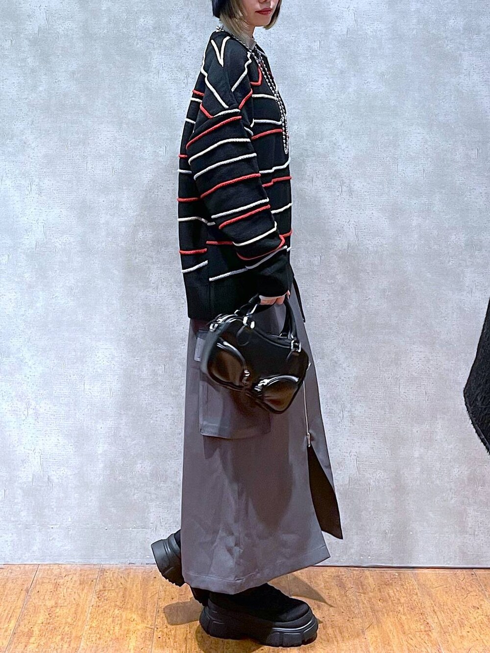 グレー系のスカート、ベージュ系のTシャツ/カットソー、ブラック系のニット/セーターを着用したレディースの冬コーディネートの2枚目の写真