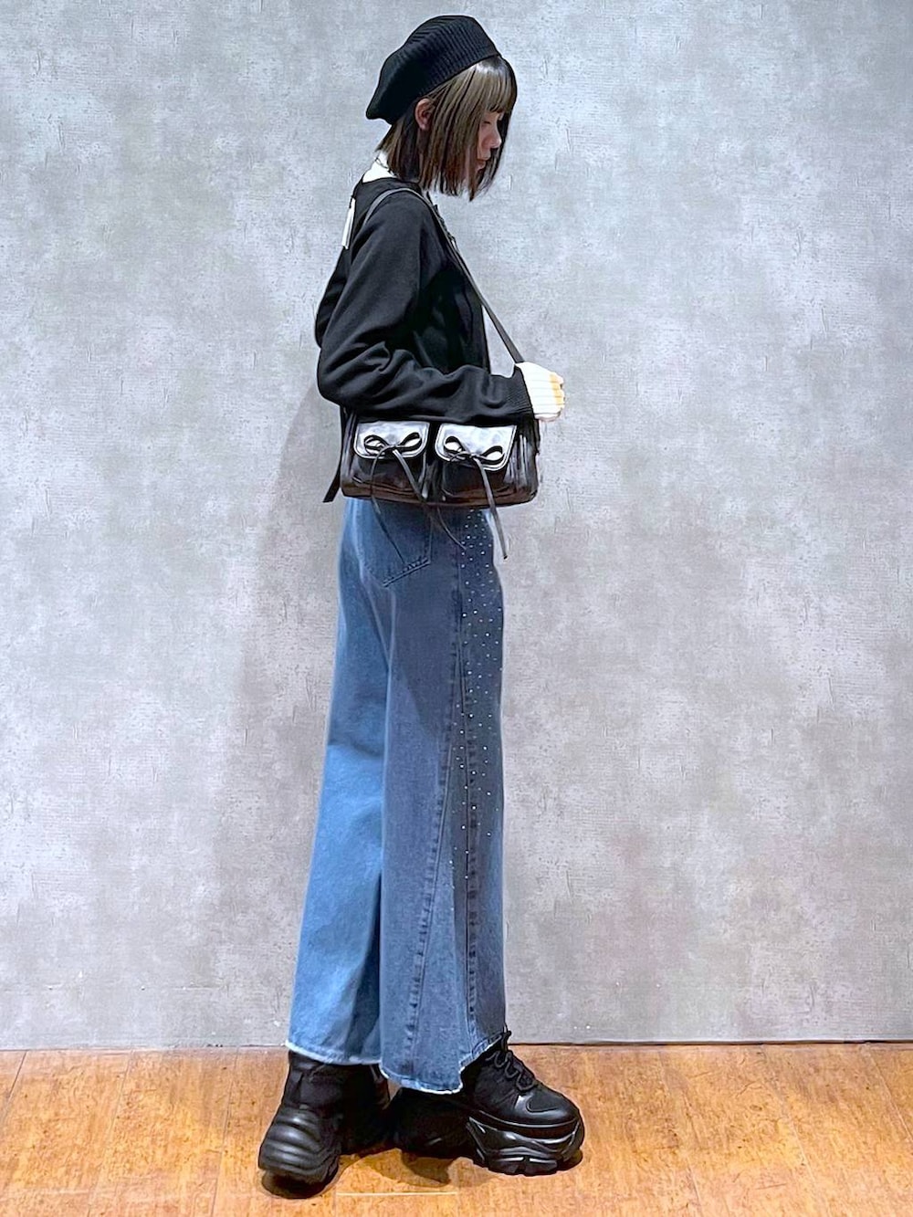 ブラック系のスニーカー、ホワイト系のニット/セーター、ブルー系のデニムパンツを着用したレディースの秋コーディネートの3枚目の写真