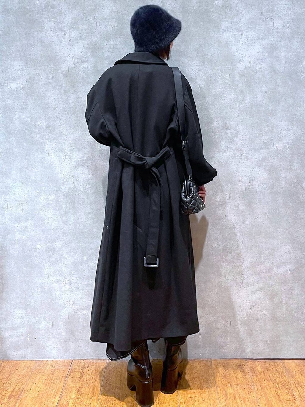 ブラック系のチェスターコート、ブラック系のブーツ、ブラック系のスカートを着用したレディースの冬コーディネートの3枚目の写真