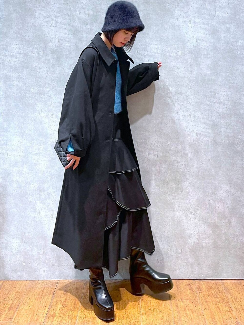 ブラック系のチェスターコート、ブラック系のブーツ、ブラック系のスカートを着用したレディースの冬コーディネートの2枚目の写真