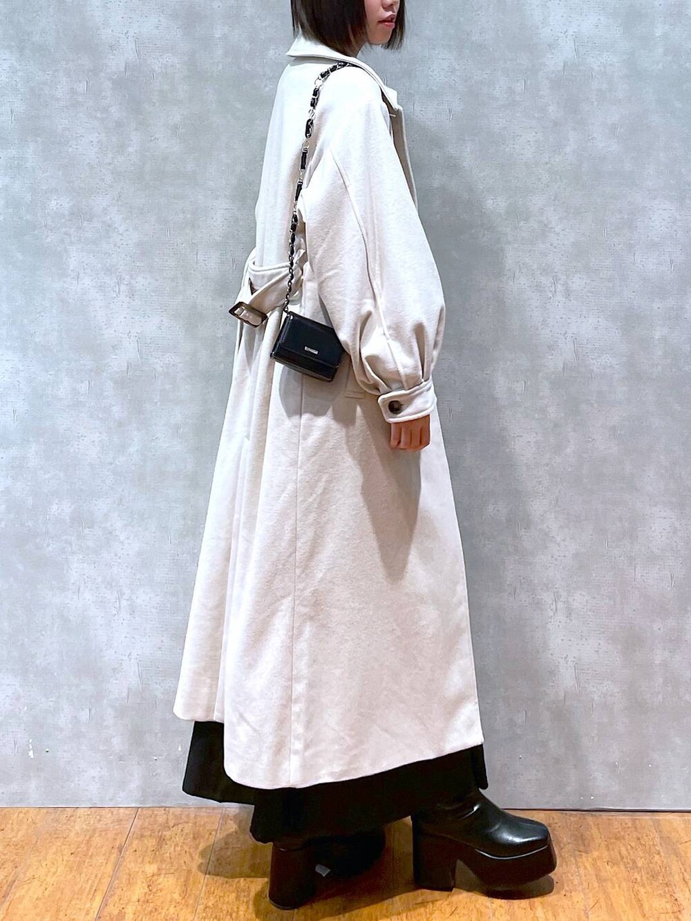 グレー系のチェスターコート、ブラック系のジャンパースカート、ブラック系のブーツを着用したレディースの冬コーディネートの3枚目の写真