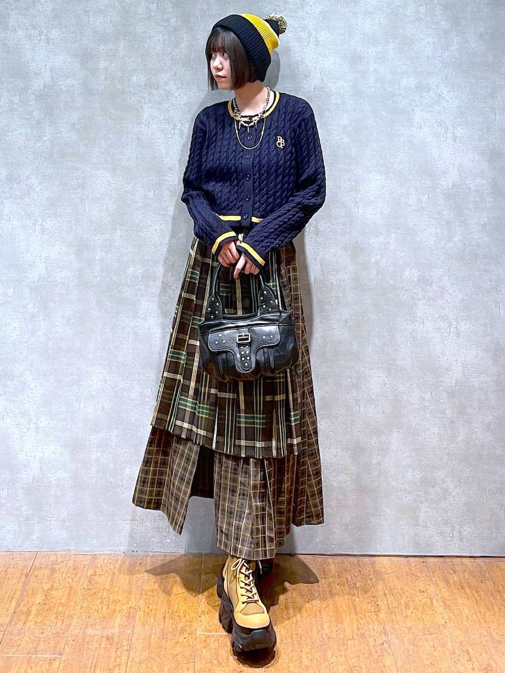 ブラウン系のブーツ、イエロー系のスカート、ブラック系のハンドバッグを着用したレディースの秋コーディネートの2枚目の写真