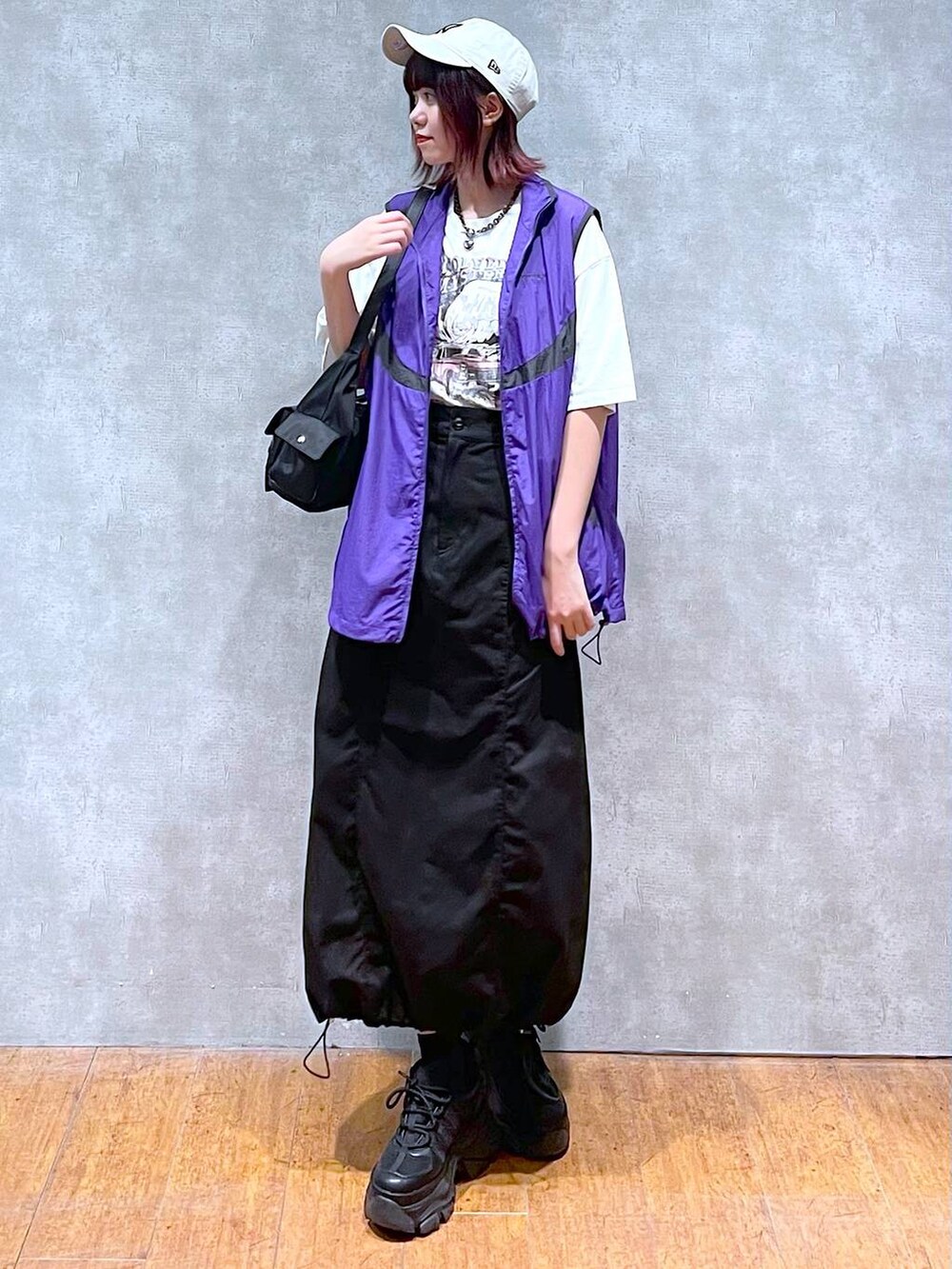 ブラック系のショルダーバッグ、ブラック系のスニーカー、パープル系のベストを着用したレディースの春コーディネートの2枚目の写真
