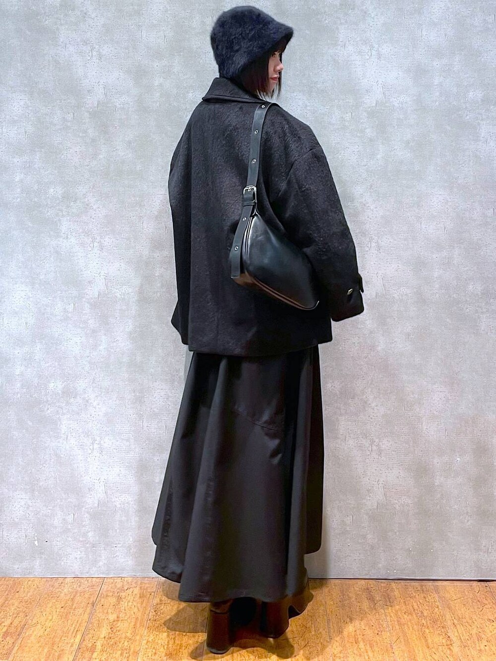 ブラック系のジャンパースカート、ブラック系のブーツ、ブラック系のショルダーバッグを着用したレディースの冬コーディネートの3枚目の写真