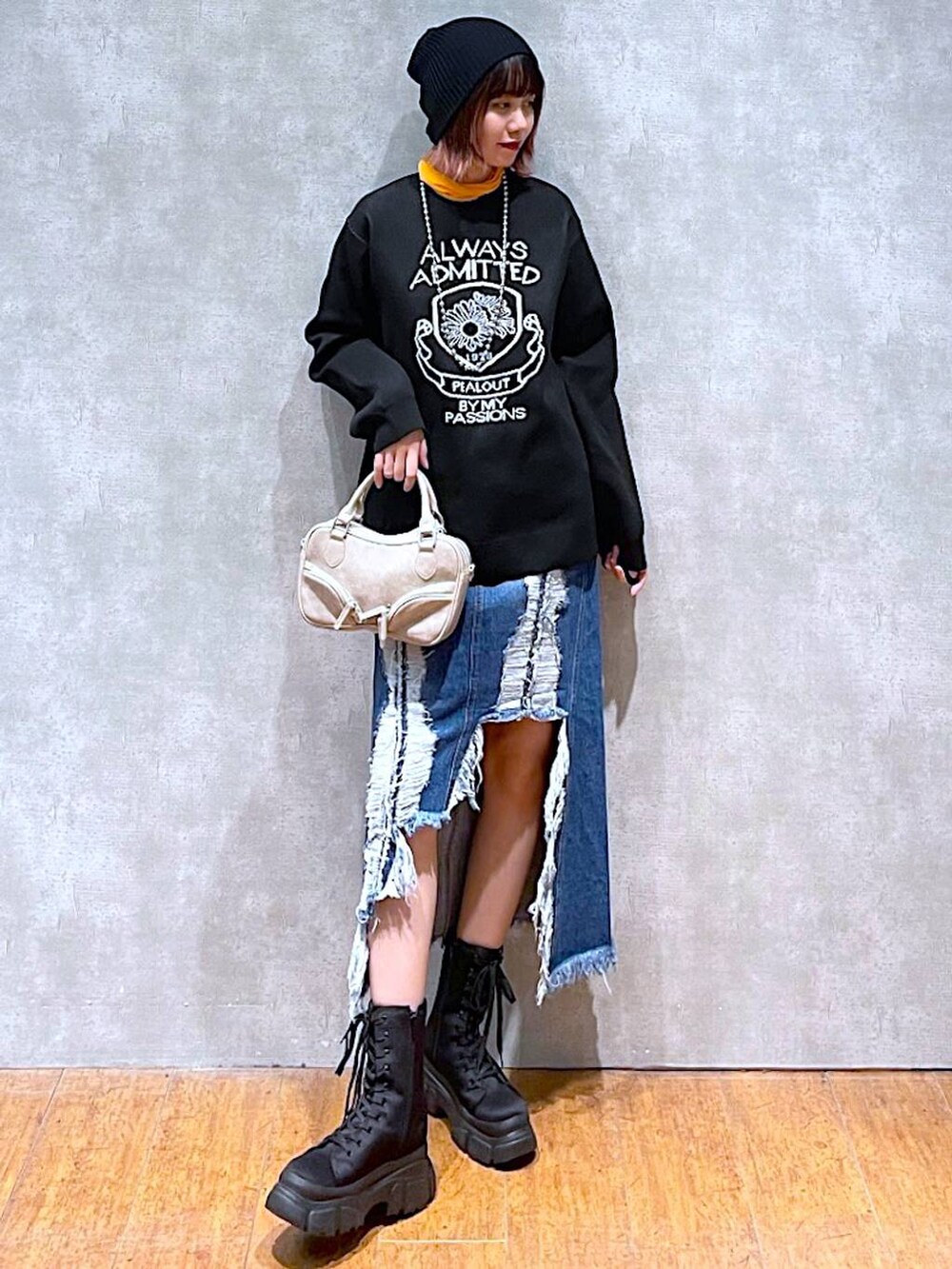 オレンジ系のTシャツ/カットソー、ブラック系のニット/セーター、ベージュ系のボストンバッグを着用したレディースの春コーディネートの2枚目の写真