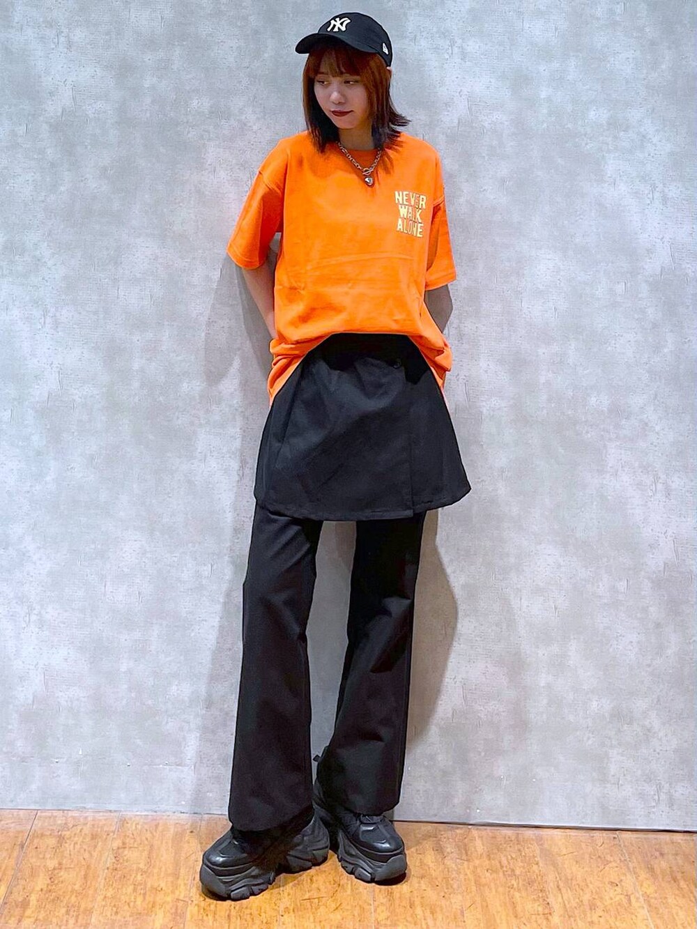 ブラック系のスニーカー、オレンジ系のTシャツ/カットソー、ブラック系のチノパンツを着用したレディースの夏コーディネートの3枚目の写真