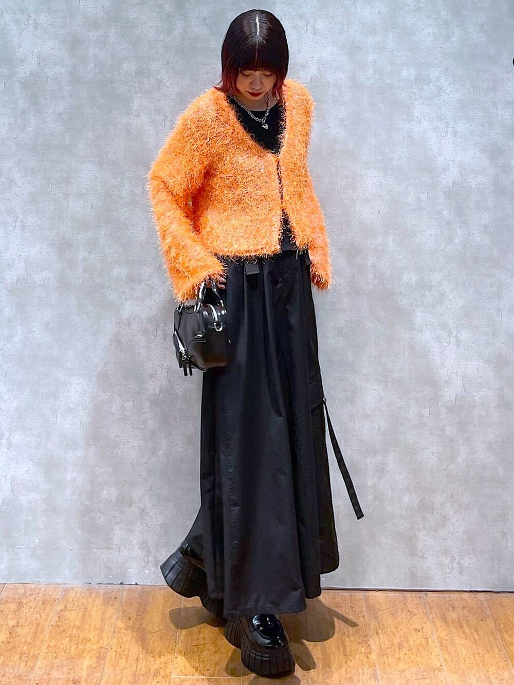 オレンジ系のカーディガン/ボレロ、ブラック系のジャンパースカート、ブラック系のローファーを着用したレディースの春コーディネートの2枚目の写真