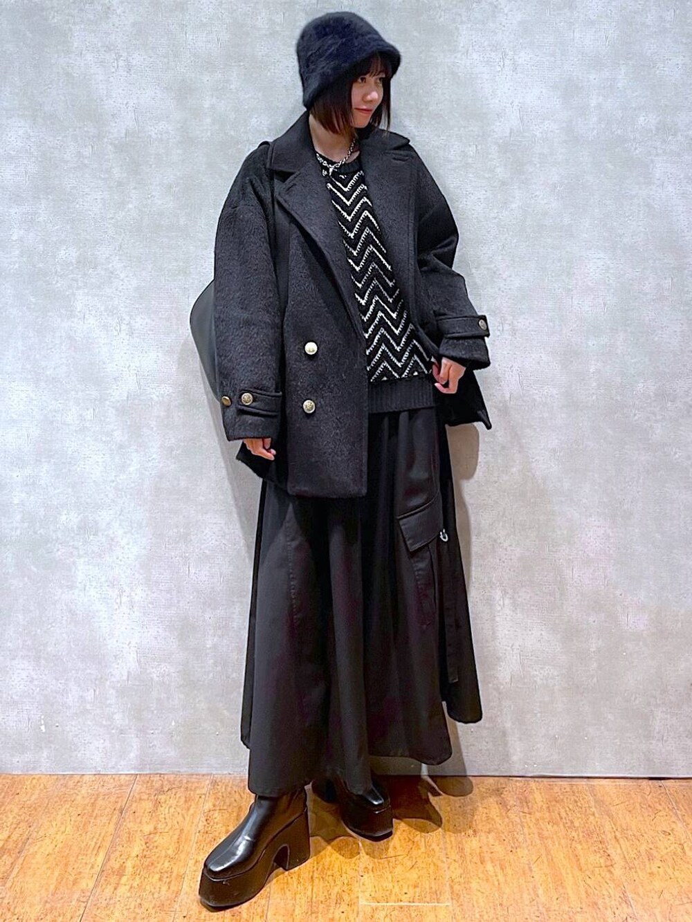 ブラック系のジャンパースカート、ブラック系のブーツ、ブラック系のショルダーバッグを着用したレディースの冬コーディネートの2枚目の写真