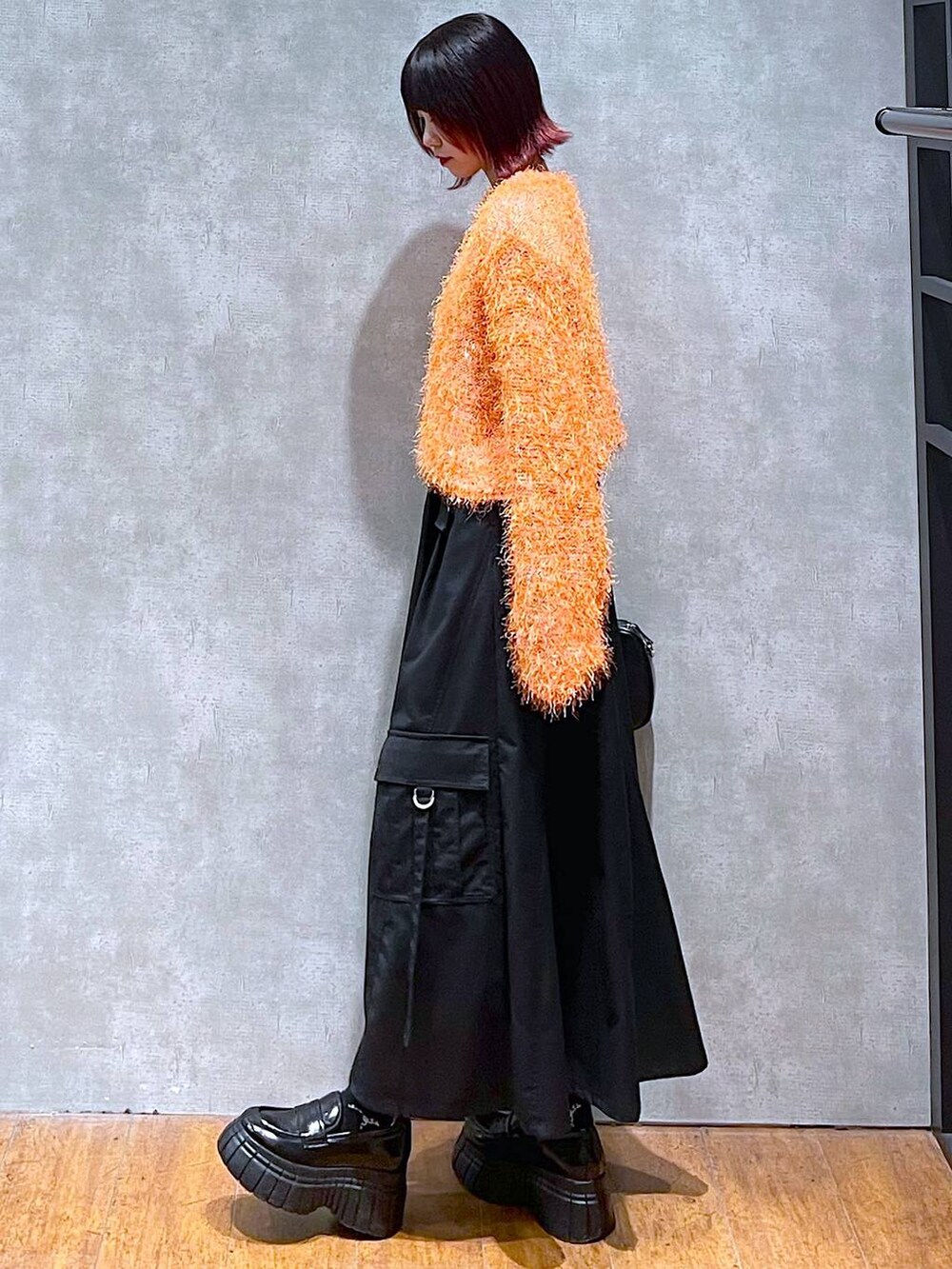 オレンジ系のカーディガン/ボレロ、ブラック系のジャンパースカート、ブラック系のローファーを着用したレディースの春コーディネートの5枚目の写真