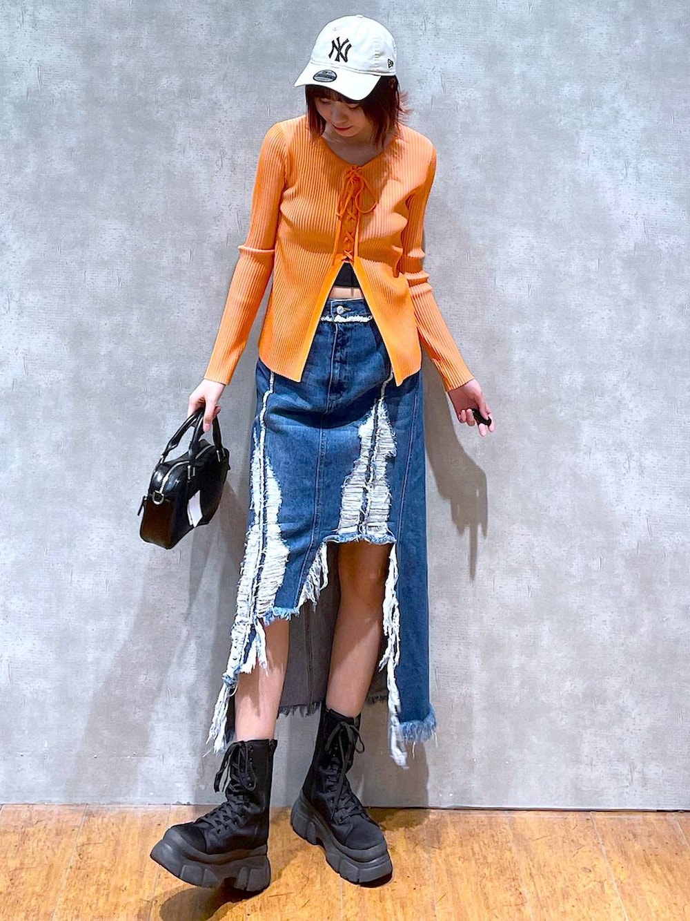 オレンジ系のニット/セーター、ブラック系のキャミソール、ブラック系のボストンバッグを着用したレディースの春コーディネートの2枚目の写真