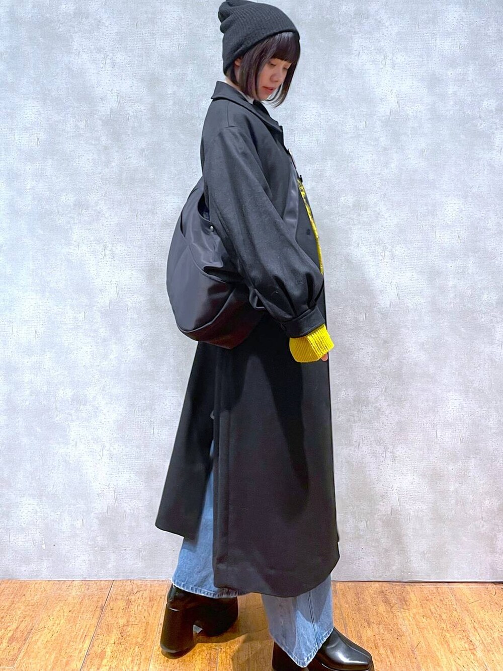 ブラック系のチェスターコート、ブルー系のデニムパンツ、イエロー系のカーディガン/ボレロを着用したレディースの冬コーディネートの3枚目の写真