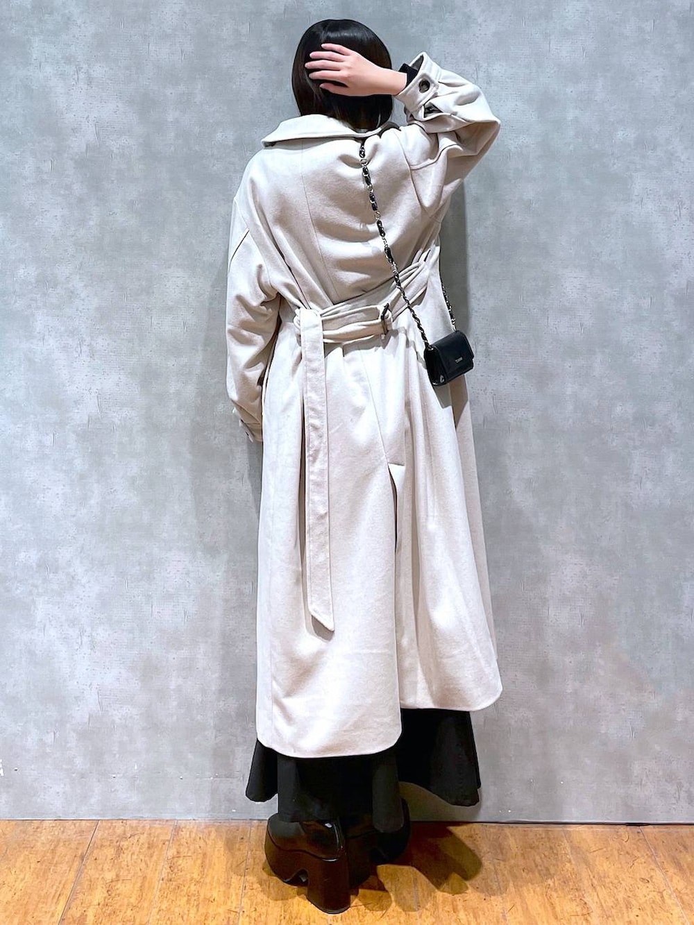 グレー系のチェスターコート、ブラック系のジャンパースカート、ブラック系のブーツを着用したレディースの冬コーディネートの2枚目の写真