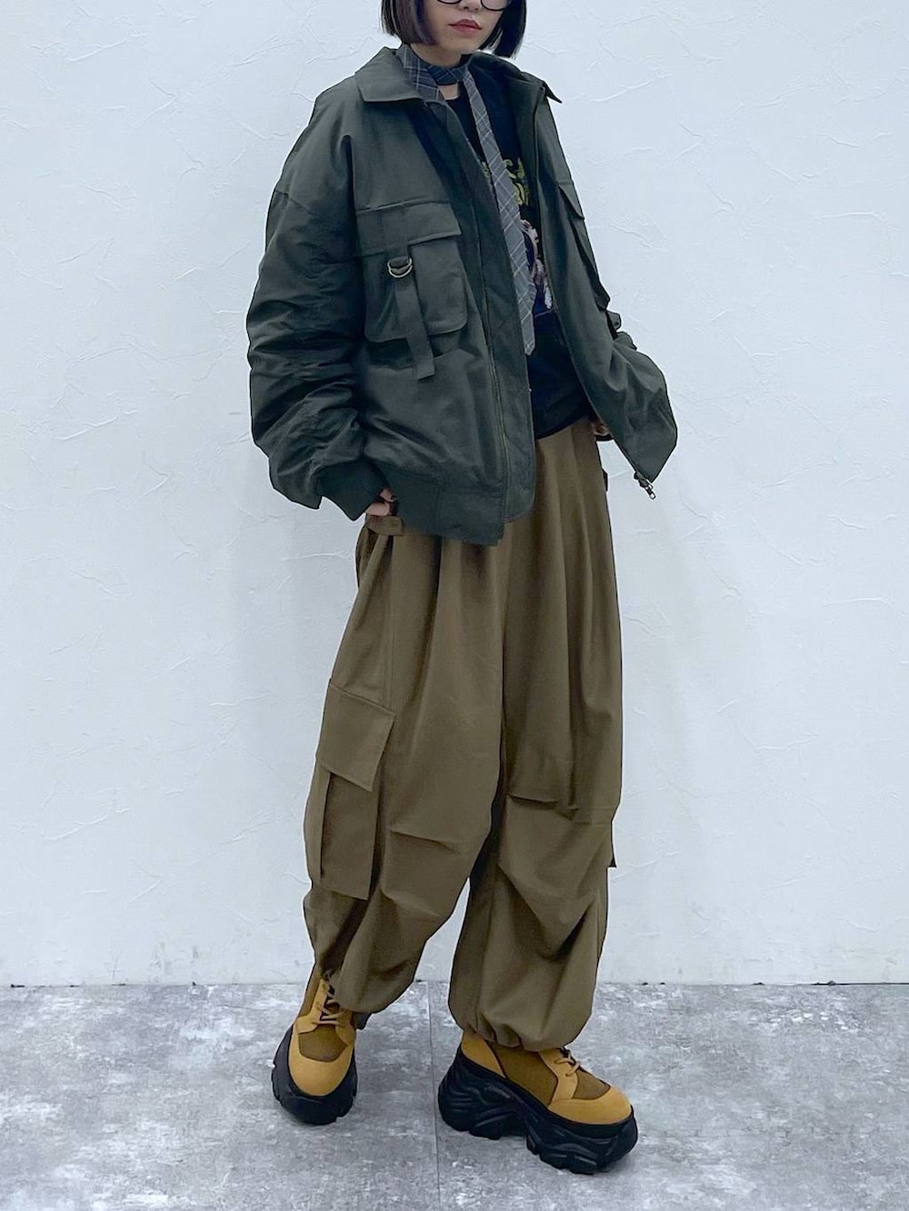 グレー系のネクタイ、ブラウン系のブーツ、グリーン系のブルゾンを着用したレディースの秋コーディネートの2枚目の写真