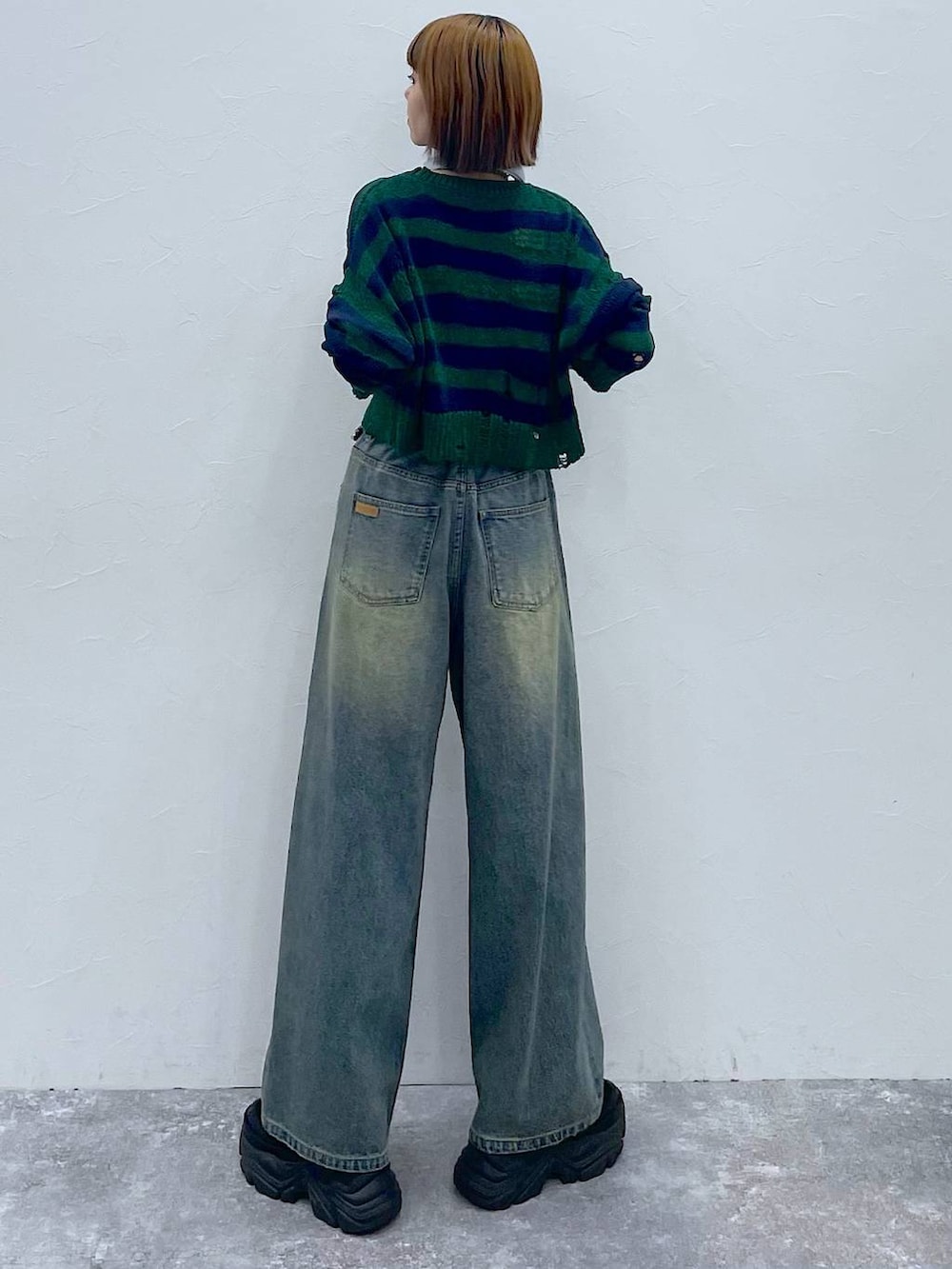 ブラック系のスニーカー、ブルー系のデニムパンツ、グリーン系のニット/セーターを着用したレディースの秋コーディネートの5枚目の写真
