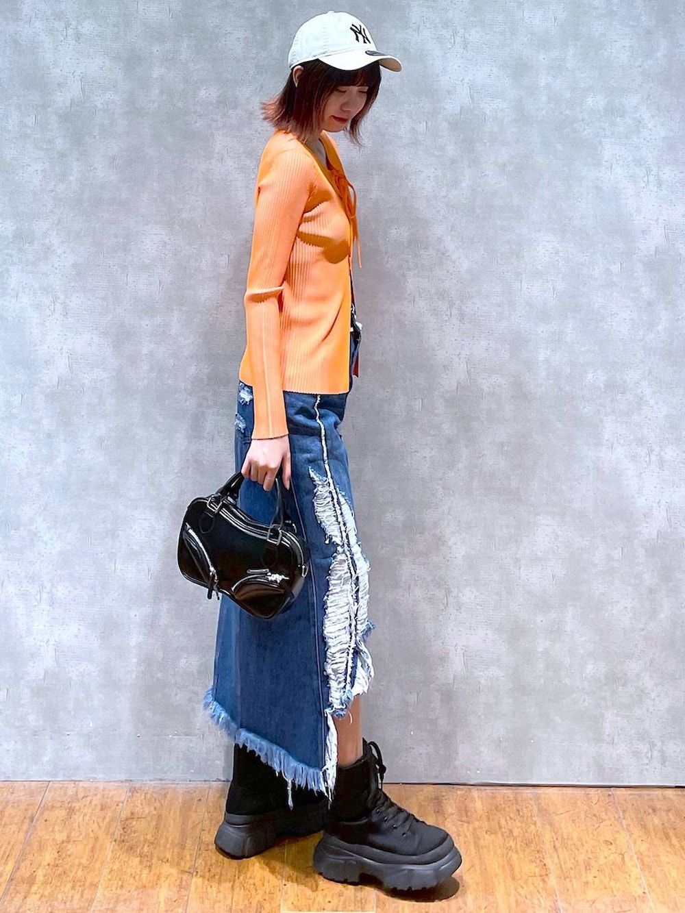 オレンジ系のニット/セーター、ブラック系のキャミソール、ブラック系のボストンバッグを着用したレディースの春コーディネートの4枚目の写真