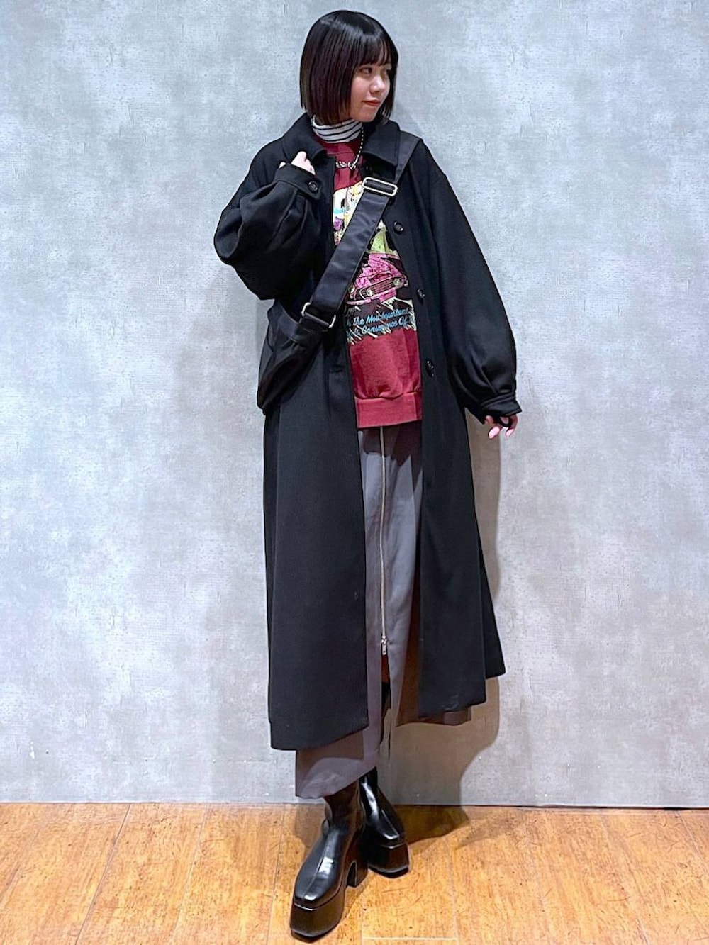 グレー系のスカート、ブラック系のチェスターコート、ブラック系のブーツを着用したレディースの冬コーディネートの2枚目の写真