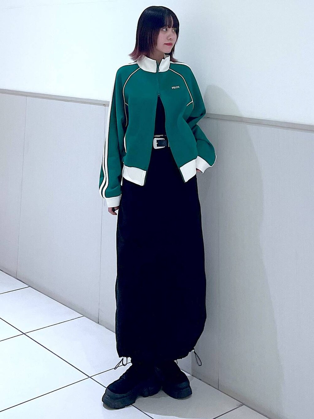 グリーン系のセットアップ、ブラック系のタンクトップ、ブラック系のブーツを着用したレディースの春コーディネートの2枚目の写真