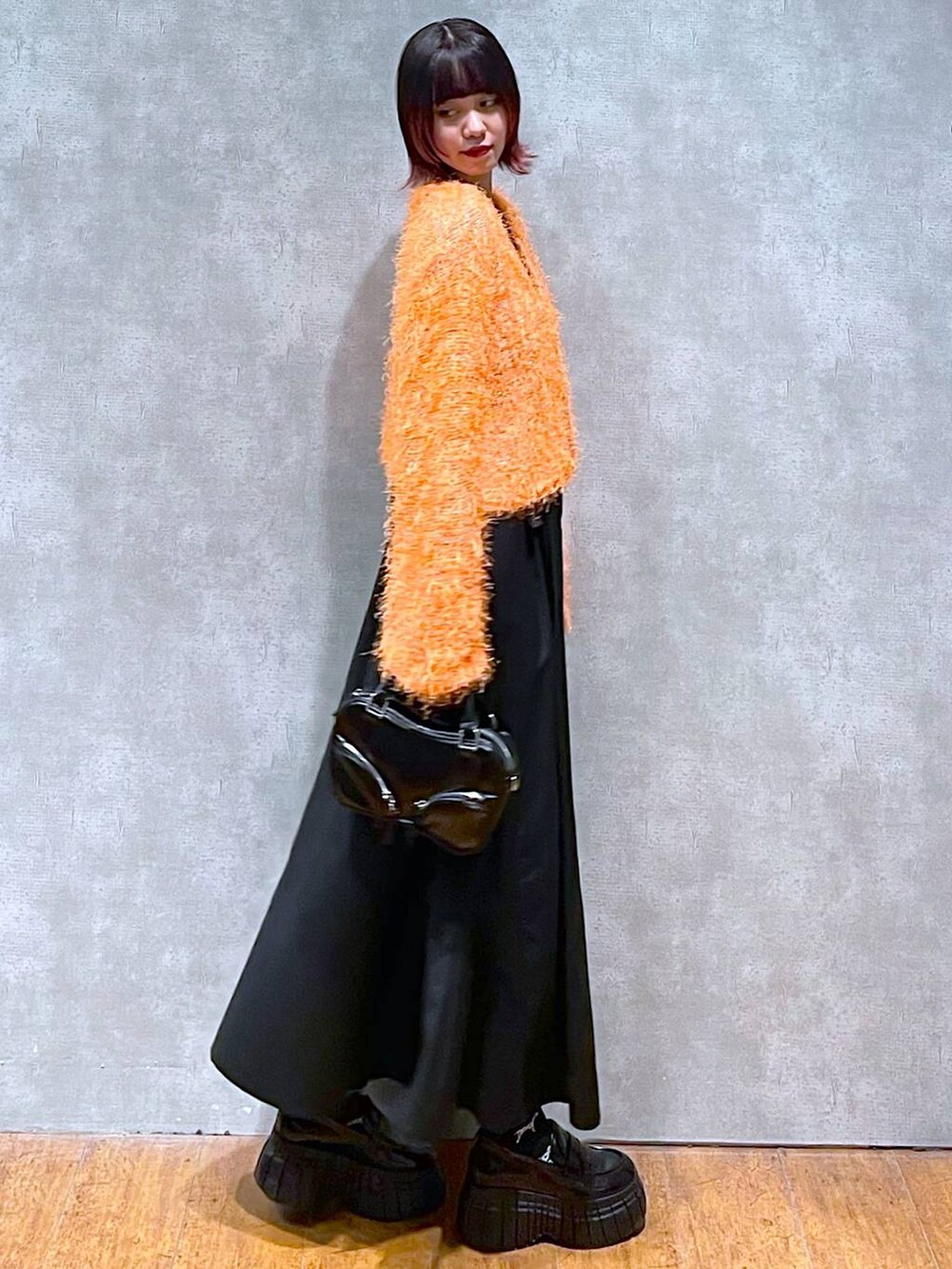 オレンジ系のカーディガン/ボレロ、ブラック系のジャンパースカート、ブラック系のローファーを着用したレディースの春コーディネートの4枚目の写真