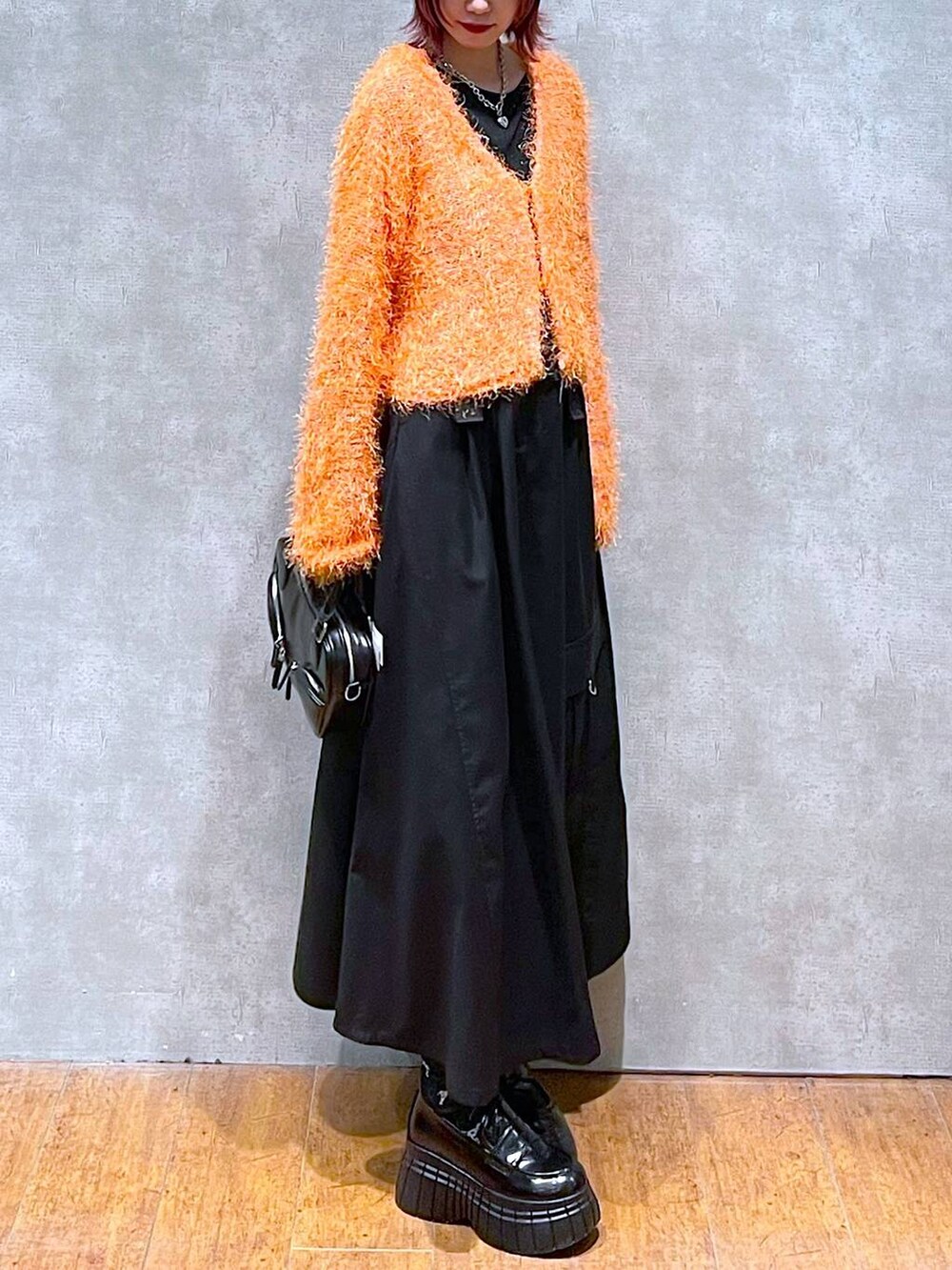 オレンジ系のカーディガン/ボレロ、ブラック系のジャンパースカート、ブラック系のローファーを着用したレディースの春コーディネートの3枚目の写真