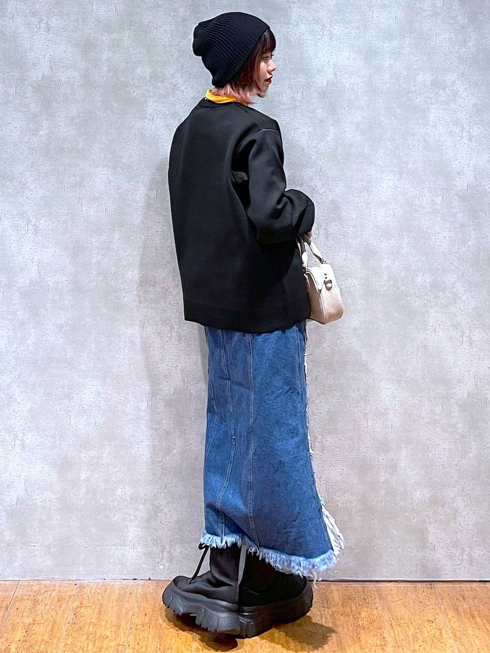 オレンジ系のTシャツ/カットソー、ブラック系のニット/セーター、ベージュ系のボストンバッグを着用したレディースの春コーディネートの4枚目の写真