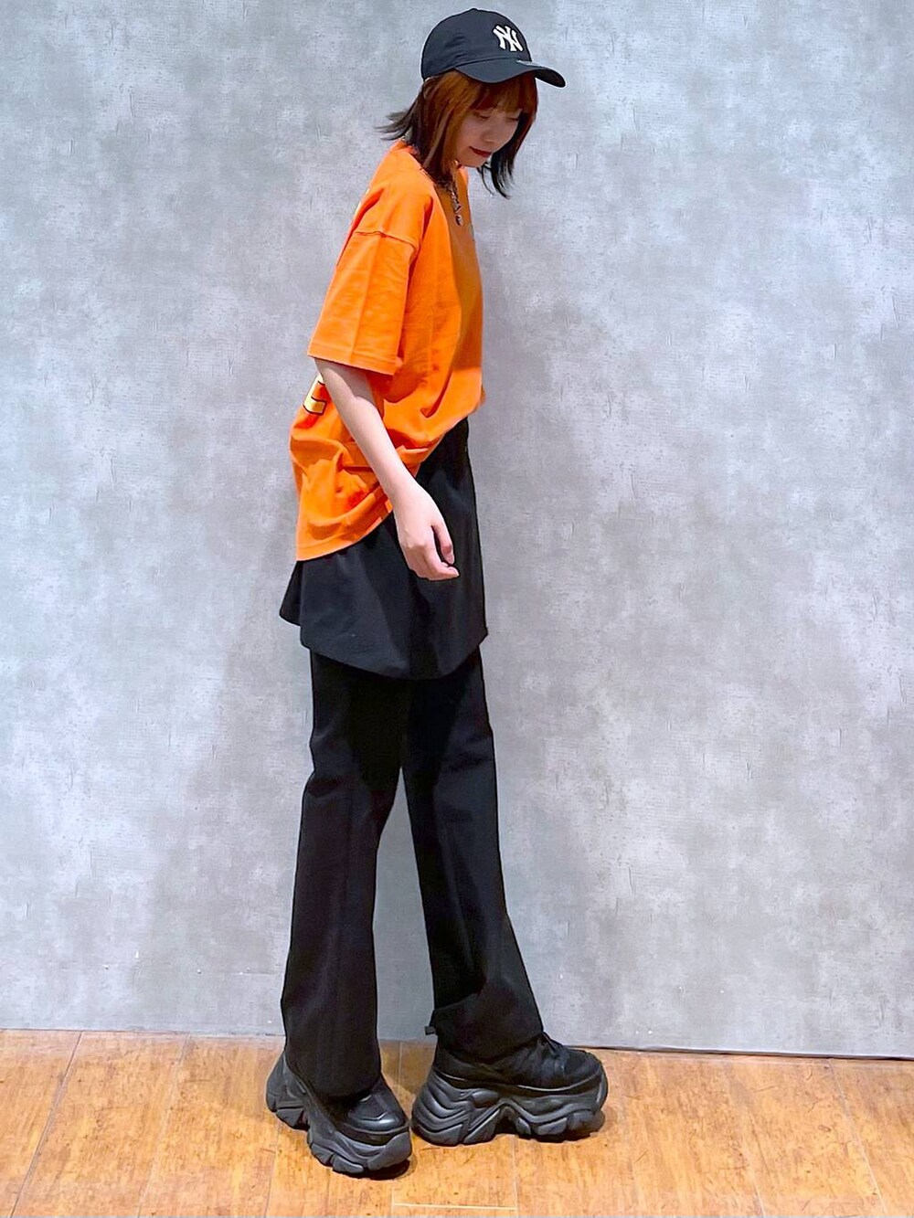 ブラック系のスニーカー、オレンジ系のTシャツ/カットソー、ブラック系のチノパンツを着用したレディースの夏コーディネートの5枚目の写真
