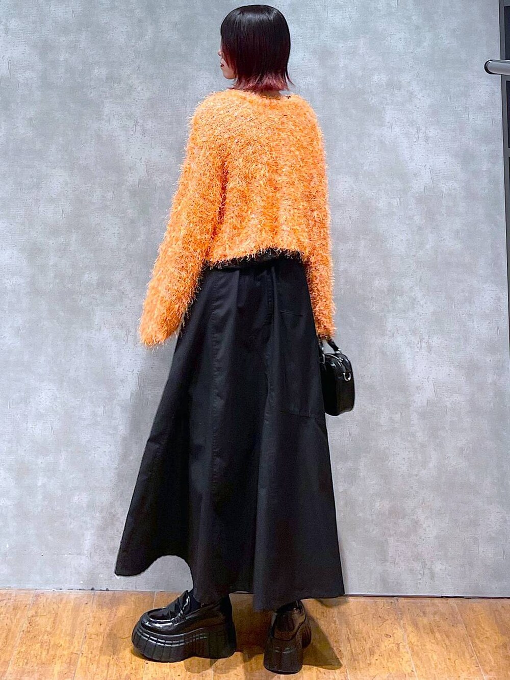 オレンジ系のカーディガン/ボレロ、ブラック系のジャンパースカート、ブラック系のローファーを着用したレディースの春コーディネートの6枚目の写真