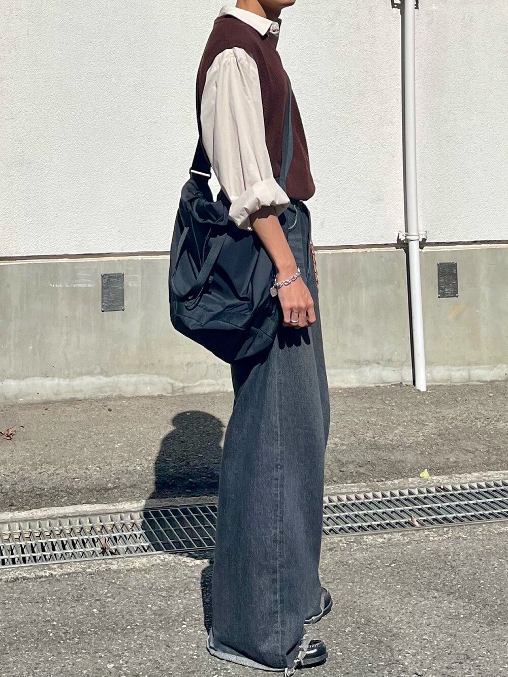ブラック系のデニムパンツ、ブラウン系のベスト、ブラック系のローファーを着用したメンズの秋コーディネートの3枚目の写真
